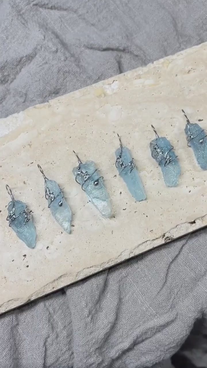 Close-up video showing several handmade glacial blue crystal necklaces, highlighting the natural shape, color variation, and one-of-a-kind character of each pendant.